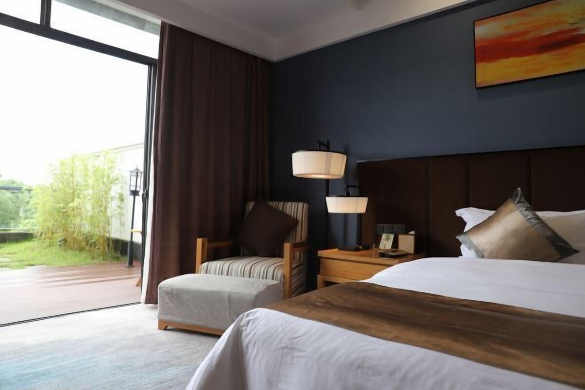 Hotellihuone, jossa on suuri sänky, tuoli, yöpöytä ja näkymä vihreälle alueelle.