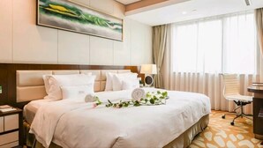 A hotel room with a large bed, a desk, a chair, and a window with curtains. - Xingtai Yuehai Hotel (Haikou)