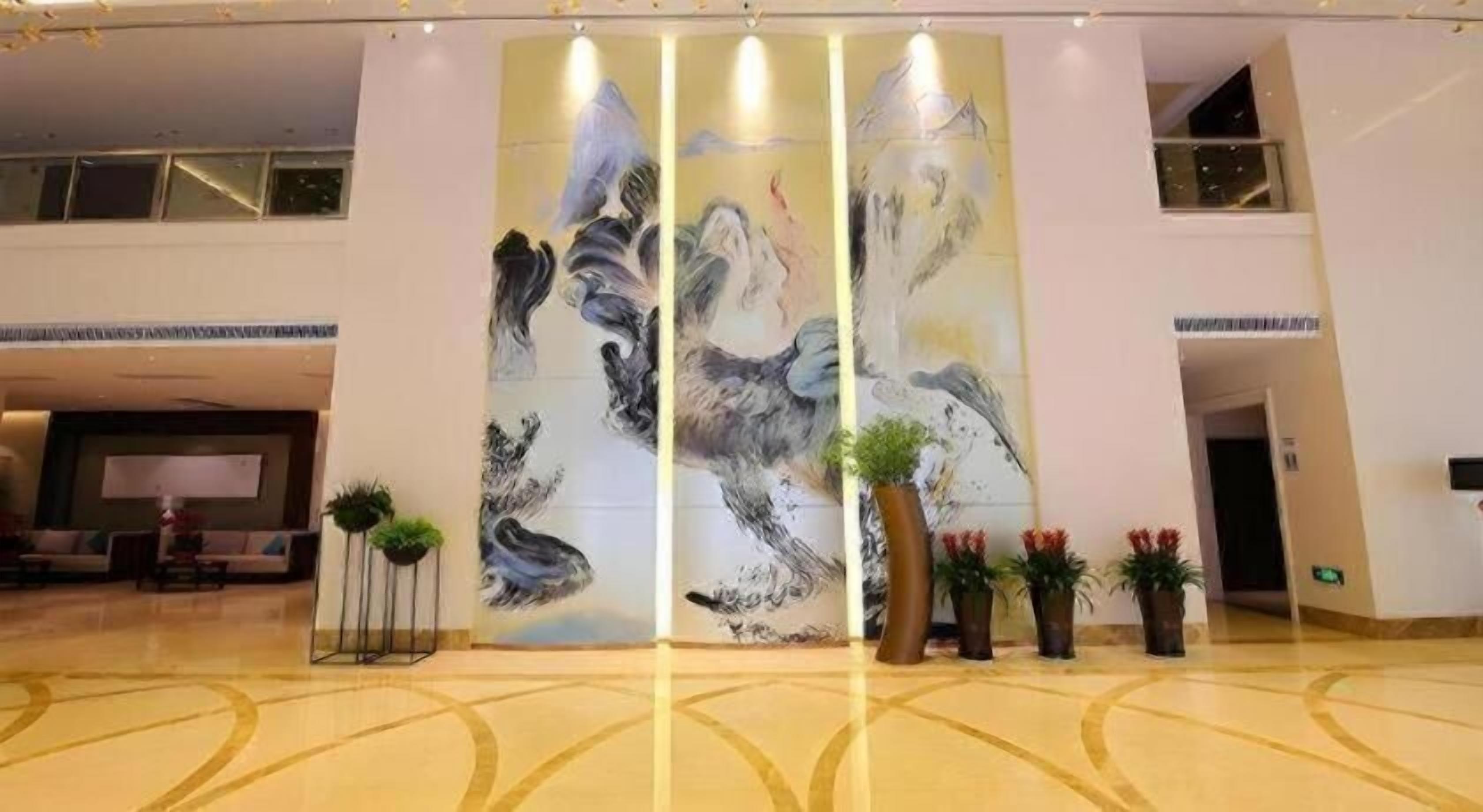 Un vestíbulo amplio con un gran mural abstracto, una mesa de recepción y varias plantas en macetas.