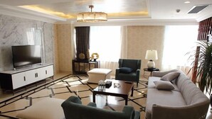 A modern living room with a flat-screen TV, a sofa, a chair, a coffee table, and a side table with a lamp. - Xingtai Yuehai Hotel (Haikou)