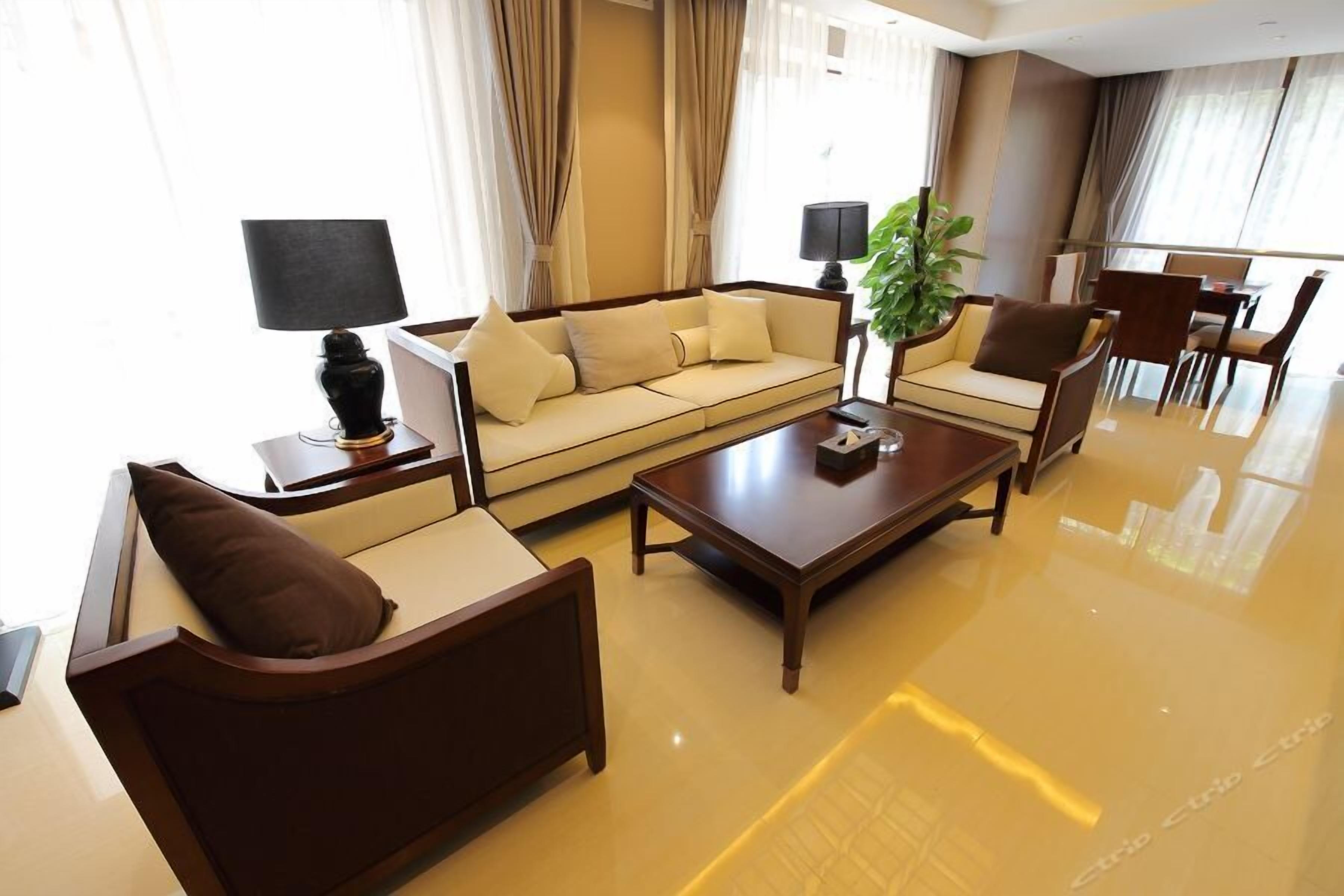 Une chambre d’hôtel moderne avec un canapé beige, une table basse en bois, un fauteuil marron et un coin repas comprenant des chaises et une table.