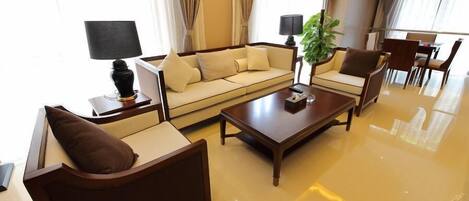Une chambre d’hôtel moderne avec un canapé beige, une table basse en bois, un fauteuil marron et un coin repas comprenant des chaises et une table.