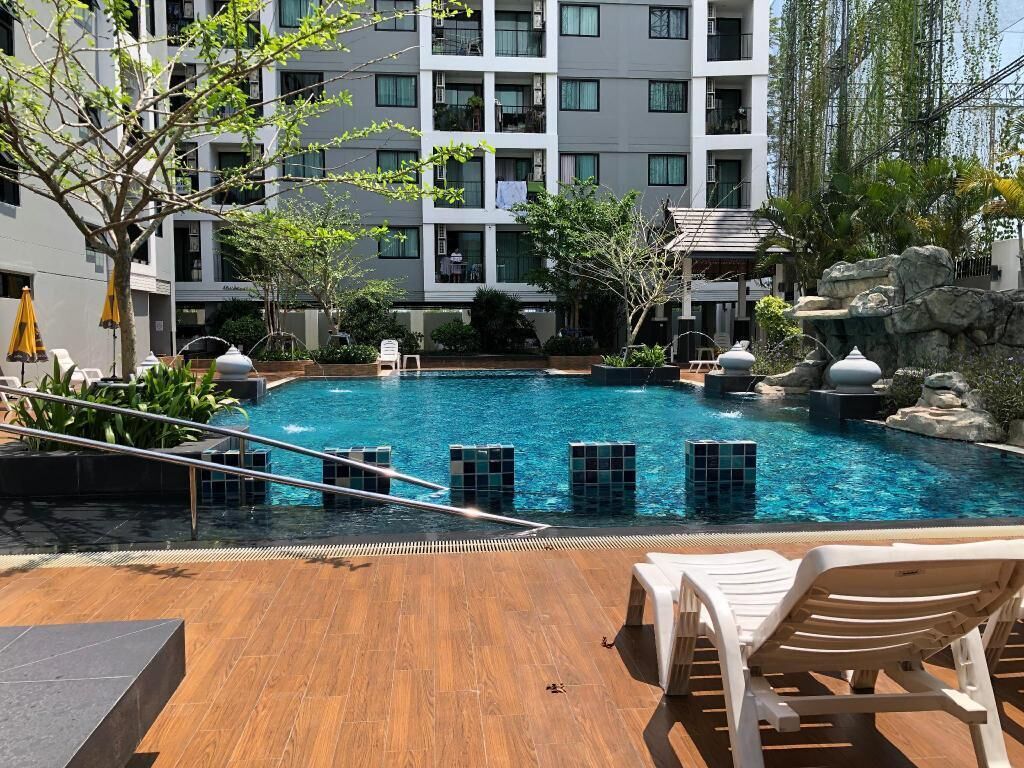 Une piscine avec une terrasse en bois, des chaises longues et un bâtiment en arrière-plan.