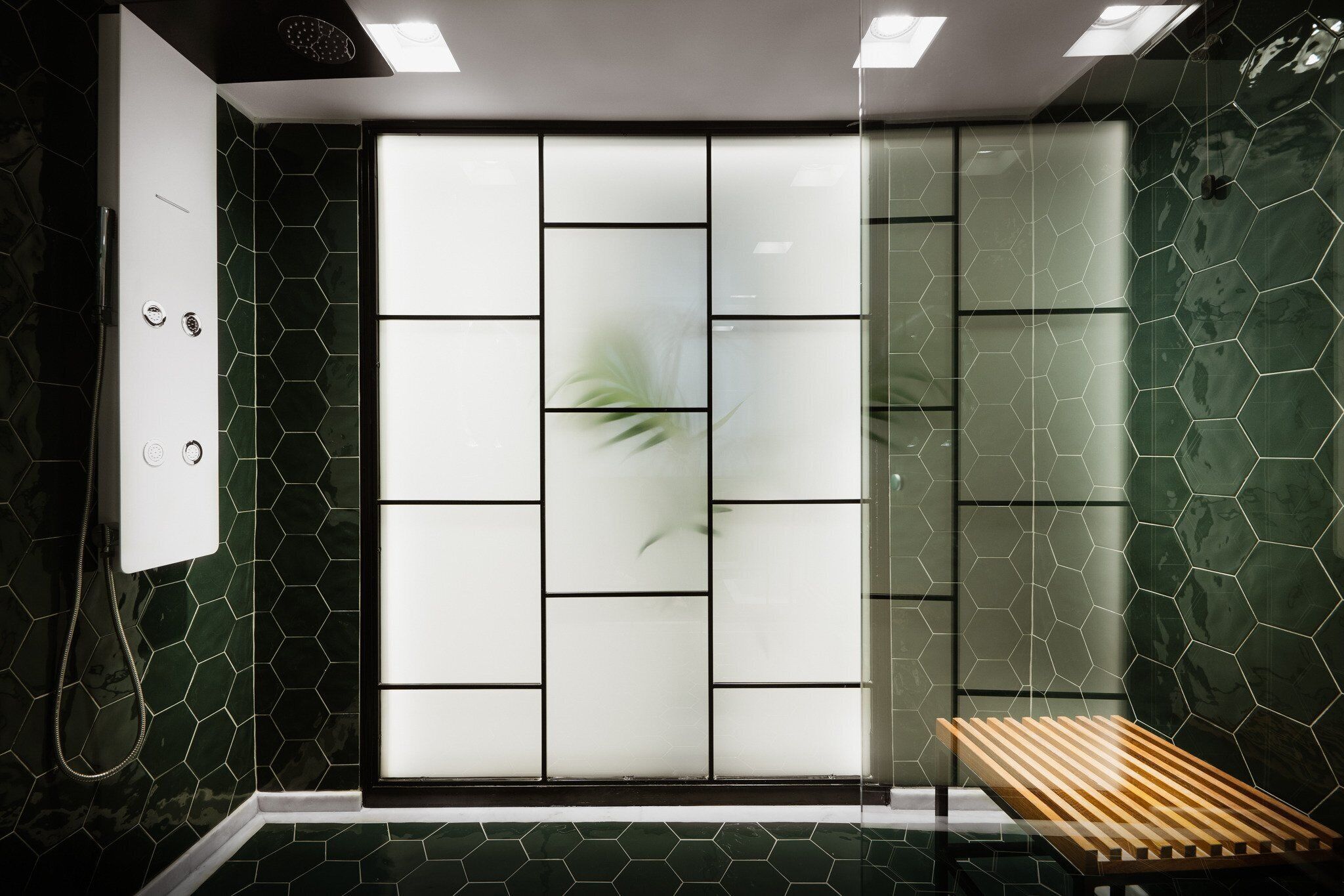 A modern bathroom with a shower, a glass partition, and a wooden bench.