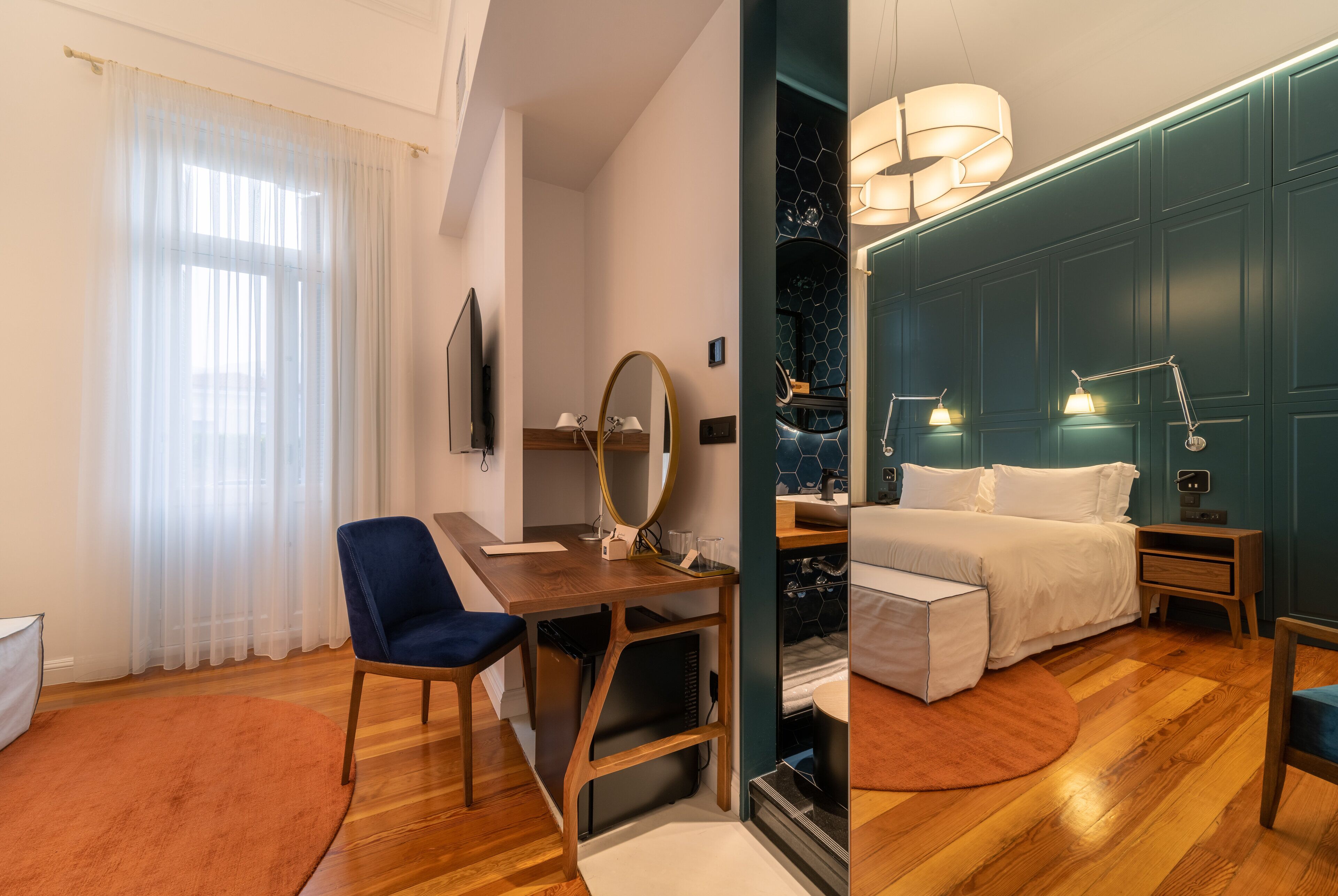 Una habitación de hotel moderna con un escritorio de madera, una silla azul, una cama con ropa blanca y una pared de acento color turquesa.