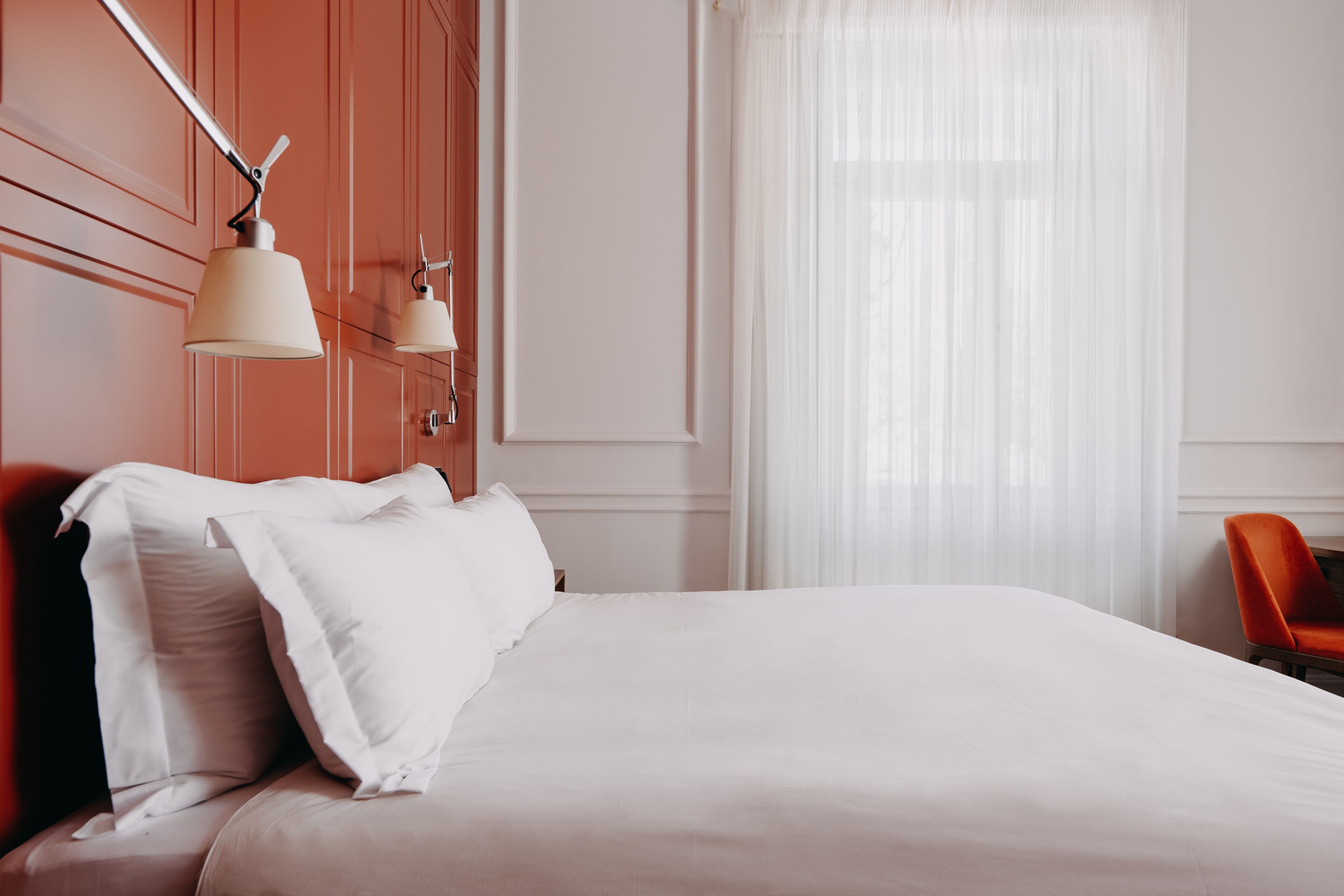 Una cama bien hecha con ropa blanca, cabecera de madera y una lámpara colgante moderna.