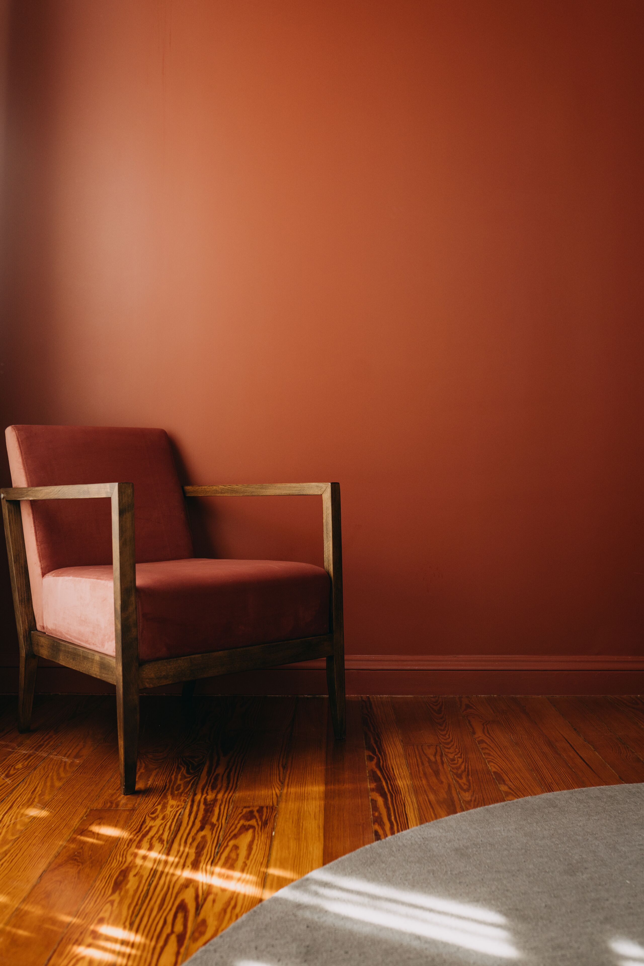 A chair with a wooden frame and a cushioned seat against a red wall, on a wooden floor.