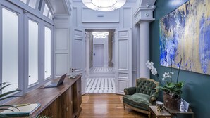 Un couloir avec un comptoir d’accueil en bois, un fauteuil vert et un grand tableau abstrait accroché au mur.