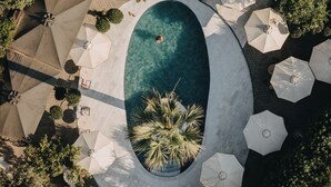 Une vue aérienne d’une piscine entourée de parasols et de palmiers.
