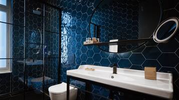 Un baño moderno con salpicadero de azulejos hexagonales negros, un lavabo blanco con un espejo encima y una zona de ducha con mampara de cristal.