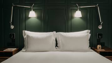 A neatly made bed with white linens, two bedside tables, and two wall-mounted reading lamps.