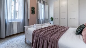A bedroom with a bed, a window with curtains, a radiator, and a wardrobe. - Wine Apartments Florence Sangiovese (Florence)