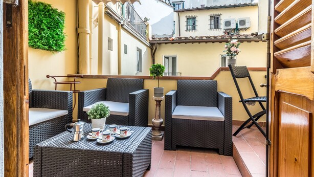 A small outdoor seating area with wicker furniture, a table with a potted plant, and a view of adjacent buildings. - Wine Apartments Florence Sangiovese (Florence)