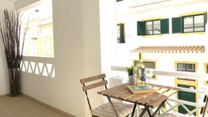 Un balcón con mesa y sillas de madera, una planta en maceta y una botella de vino.
