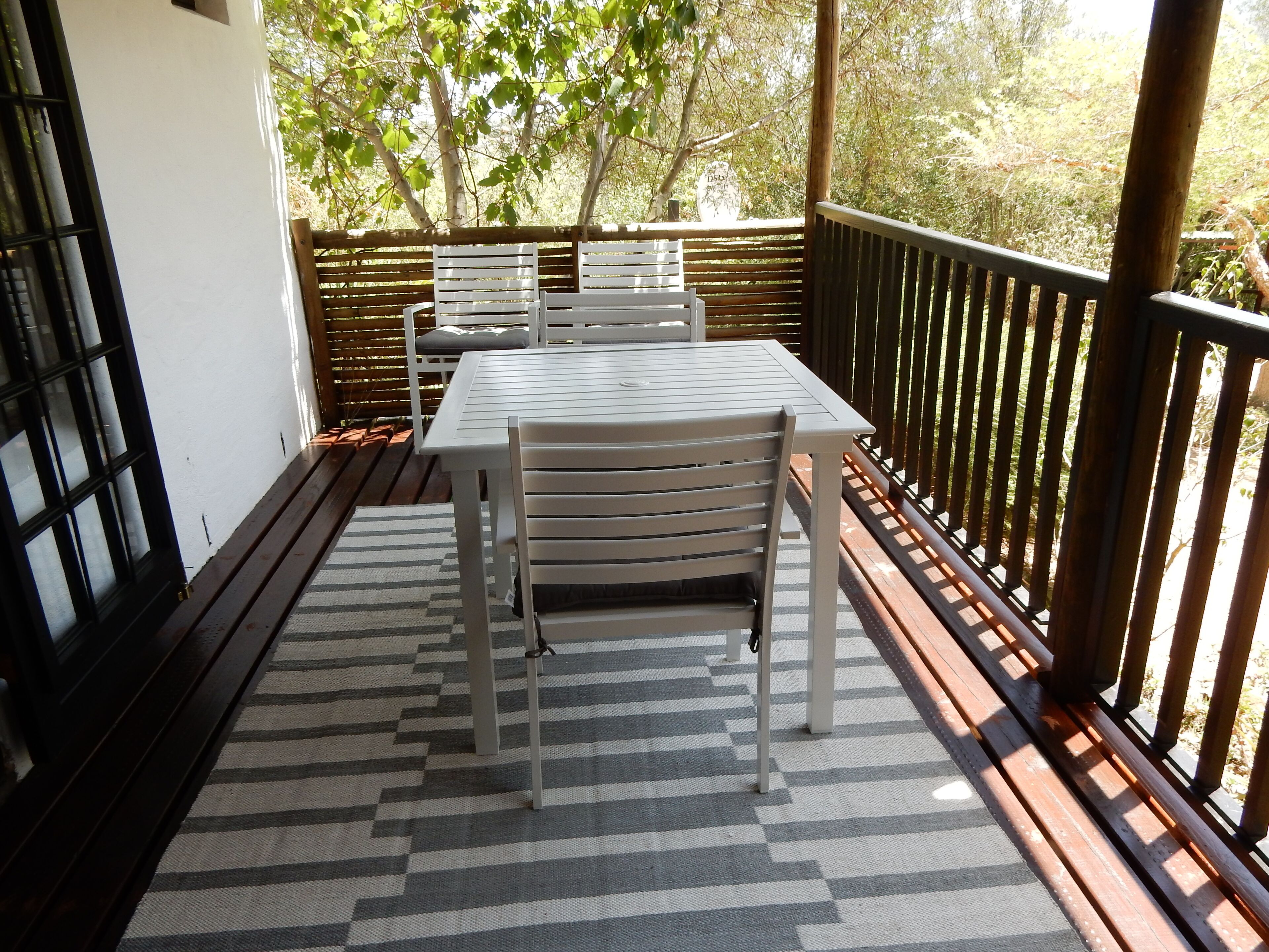 A balcony with a table and chairs, a patterned rug, and a wooden fence.