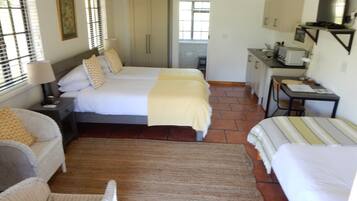 Een hotelkamer met drie bedden, een bureau, een stoel en een kleine kitchenette.