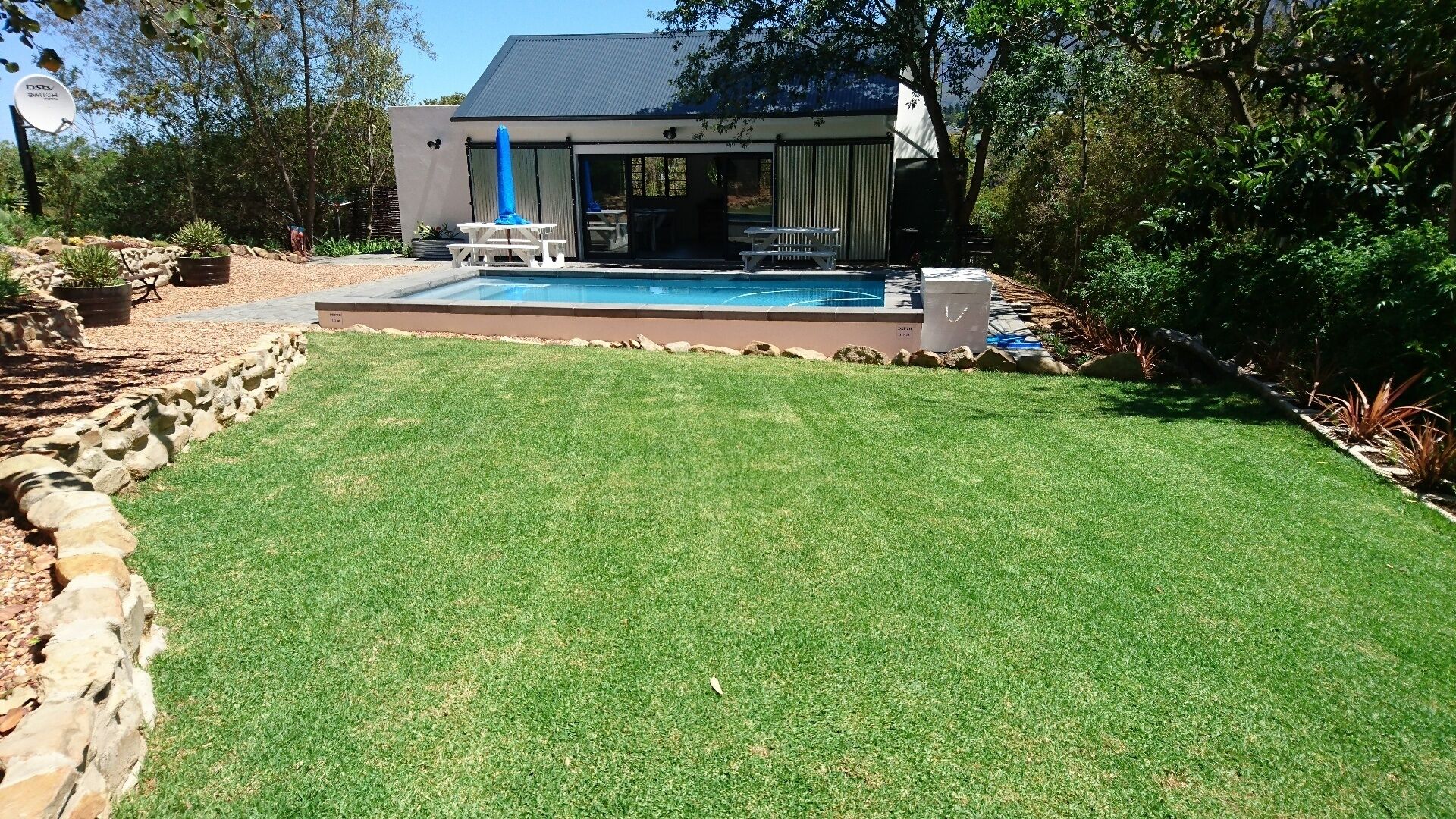 A backyard with a swimming pool, a patio with seating, and a house with a blue roof.