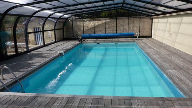 An indoor swimming pool with a wooden deck and a covered roof structure. - Domaine de la Hurel (Valambray)