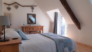 A bedroom with a sloped ceiling, a wooden dresser, a bed with a blue and white checkered blanket, a mirror, and decorative heart-shaped wall hangings. - Spacious rural gite near Malestroit, Brittany - sleeps 6 (Ruffiac)