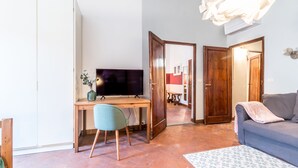 A living room with a sofa, a TV, a desk, and a chair. There are two doors leading to other rooms. - Wine Apartments Florence Franciacorta (Florence)