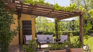 An outdoor patio with a pergola, two cushioned chairs, a table, and potted plants. - Villa San Marco (Fratte Rosa)