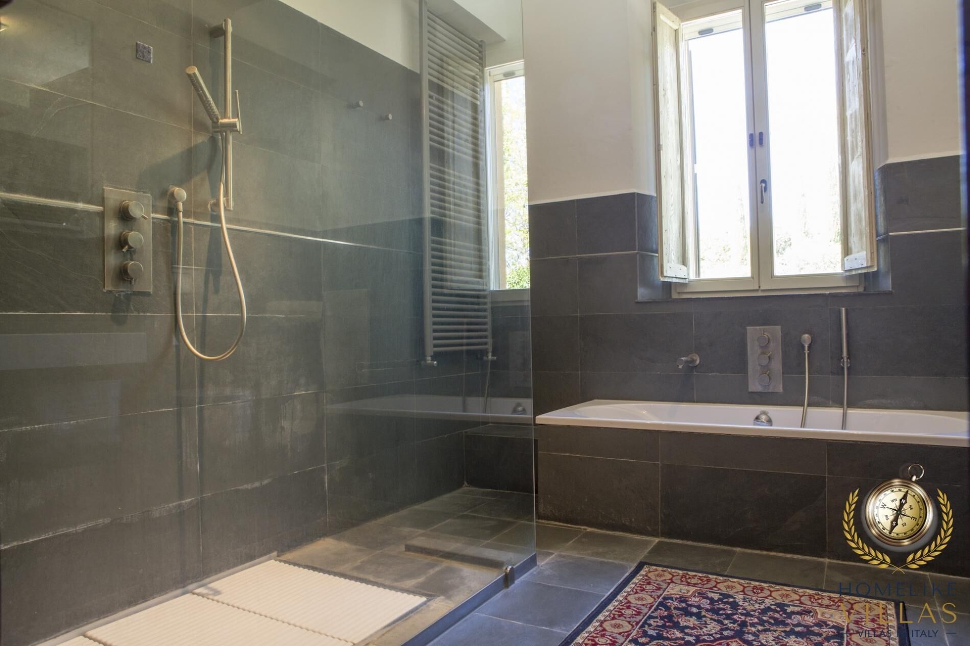 A modern bathroom with a glass-enclosed shower, a large bathtub, and a window providing natural light.