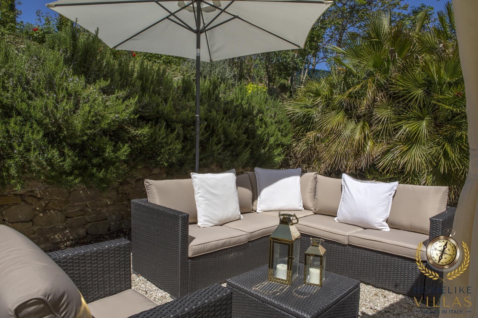 A wicker sofa with cushions, a matching ottoman, and two lanterns on a table.