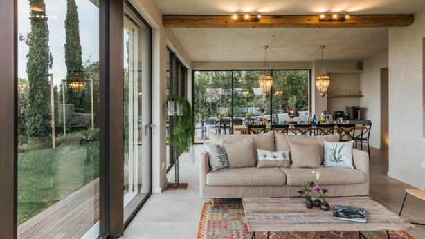 A modern living room with a large window, a sofa, a coffee table, and a dining area visible through the glass. - Villa Sogno Adriatico (Civitanova Marche)