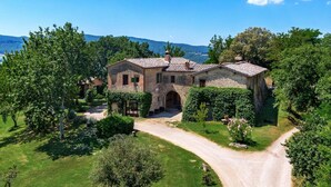 A stone house with a tiled roof, surrounded by lush greenery and a winding driveway. - Villa Murlo (Buonconvento)
