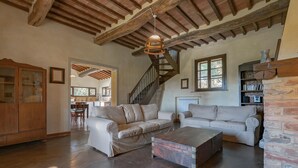 A spacious living room with a high ceiling, exposed wooden beams, a staircase, and a cozy fireplace. - Villa Murlo (Buonconvento)