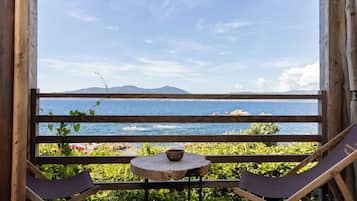 A wooden deck with a table and two chairs, overlooking a body of water and distant mountains.