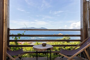 A wooden deck with a table and two chairs, overlooking a body of water and distant mountains. - Villa Kirssis (Pietrosella)