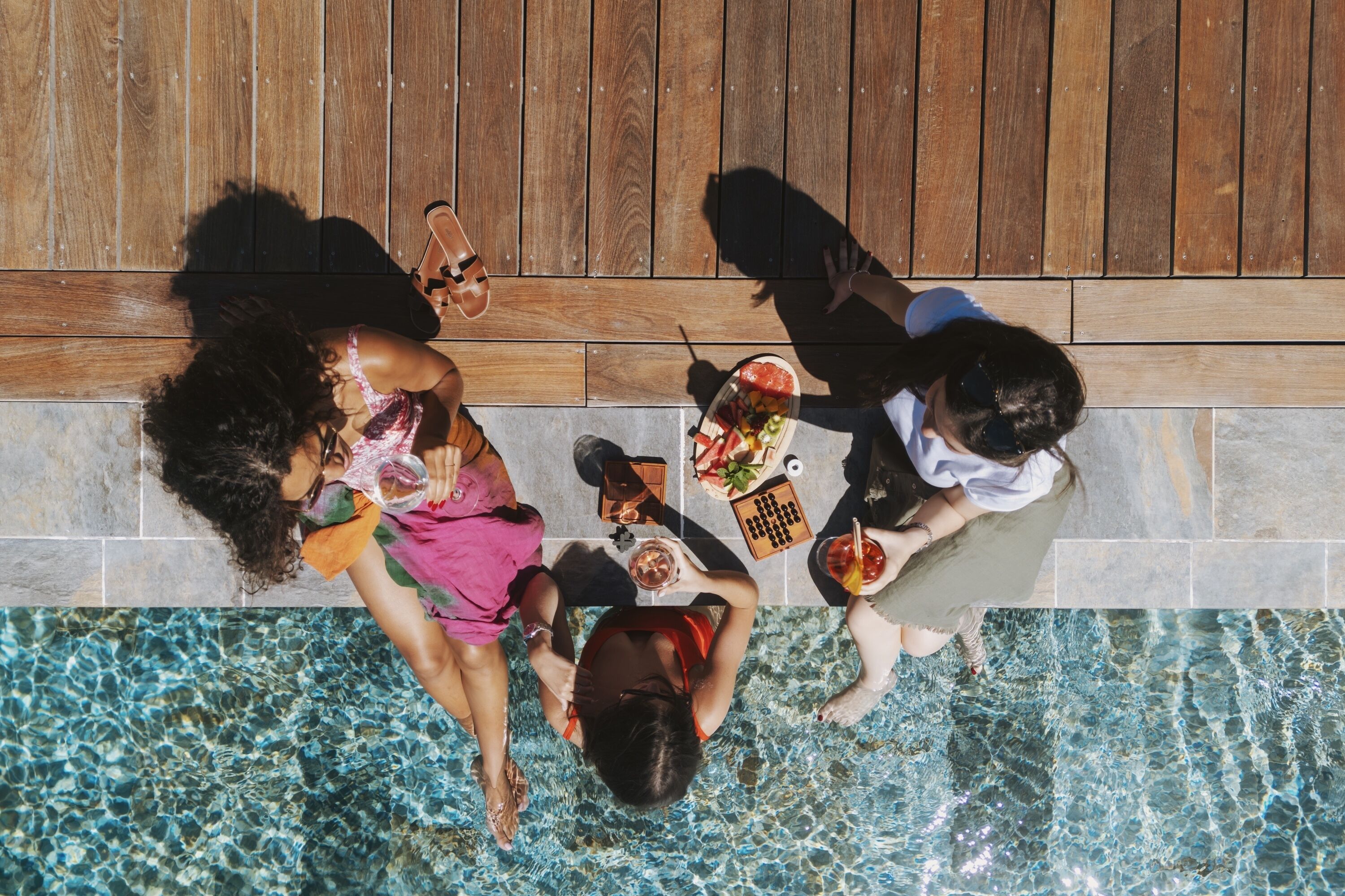 A top-down view of a poolside area with a wooden deck and a tiled pool.
