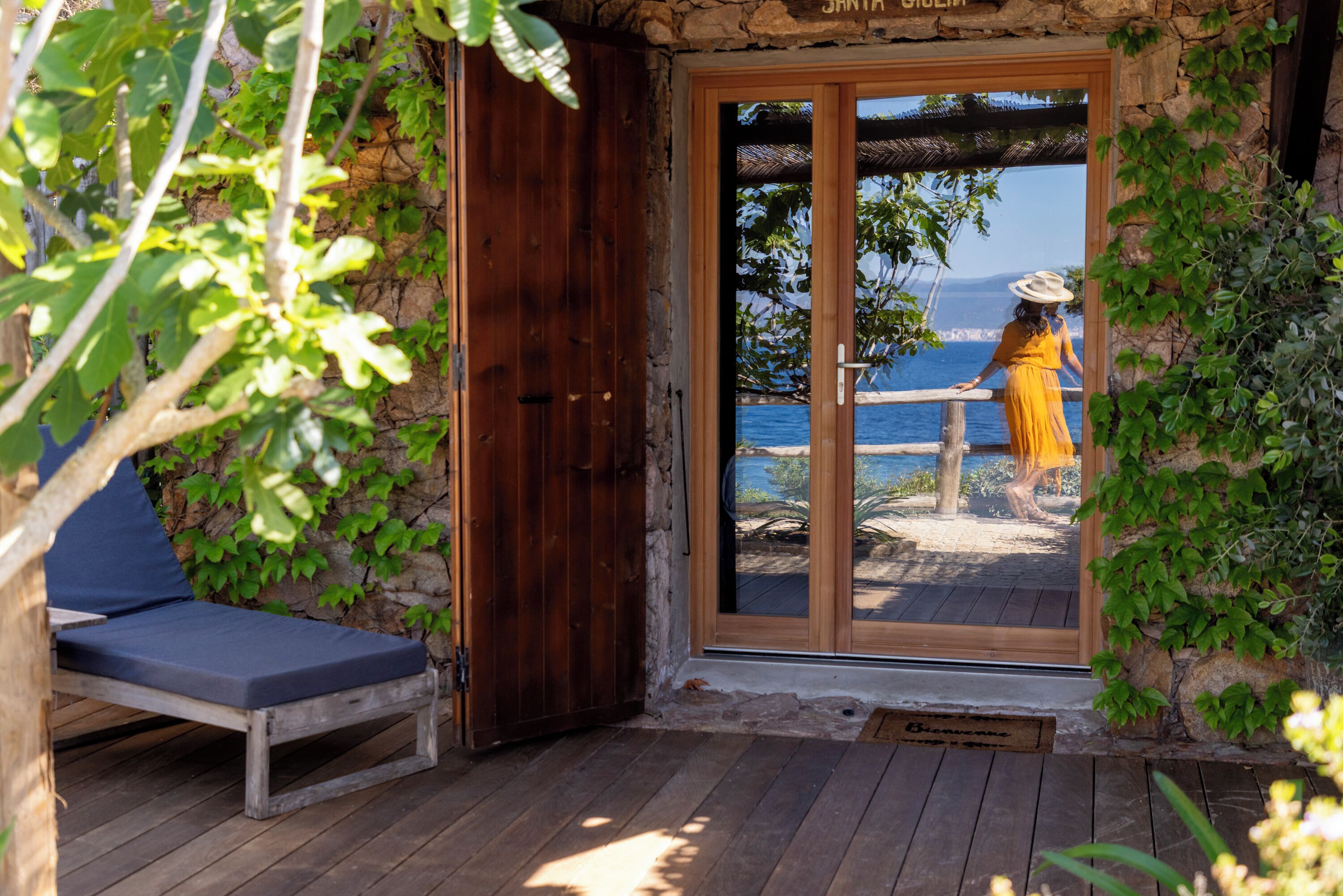 A wooden deck with a bench, a stone wall, and a view of the sea.