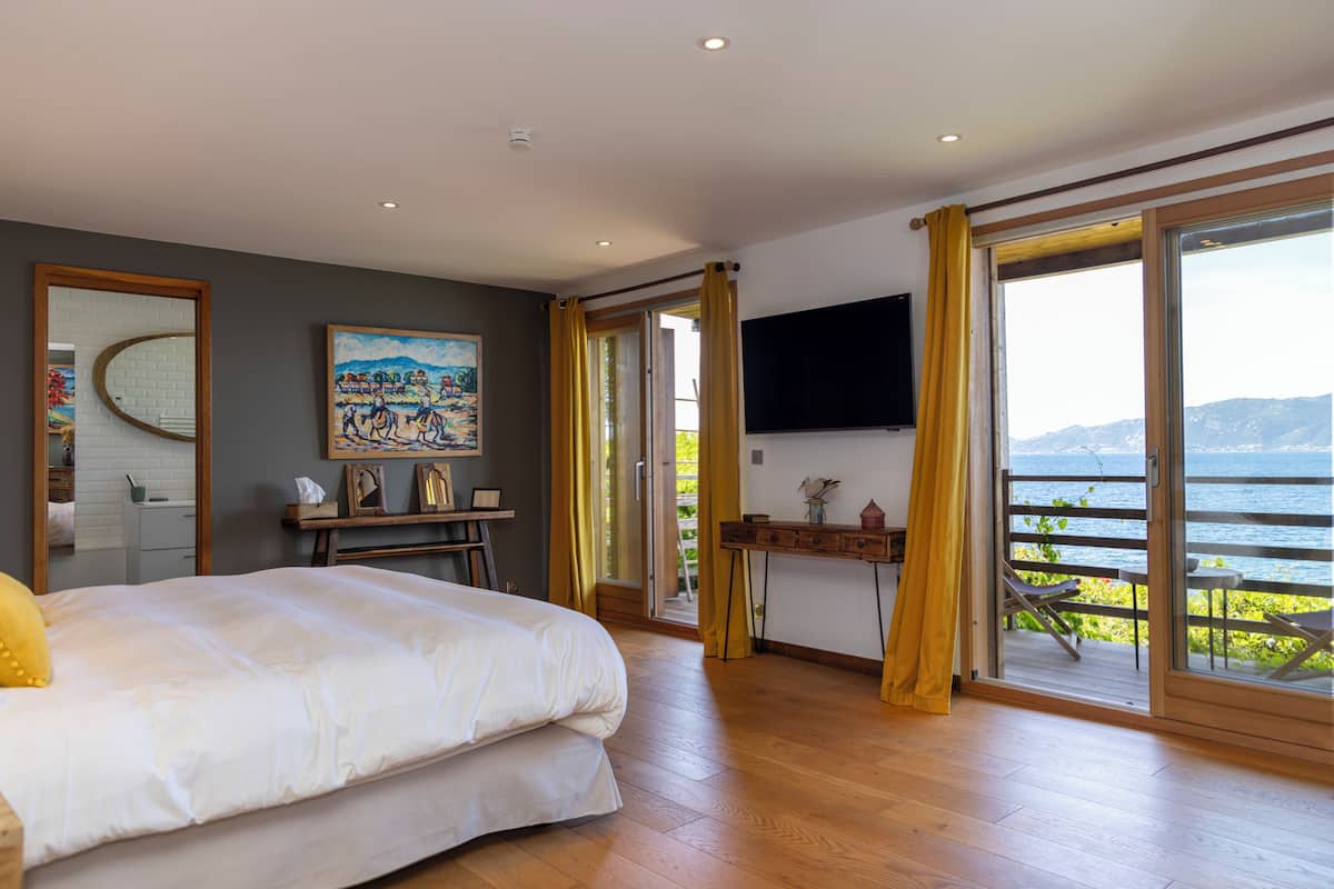 A bedroom with a bed, a desk, a TV, and a balcony with a view.