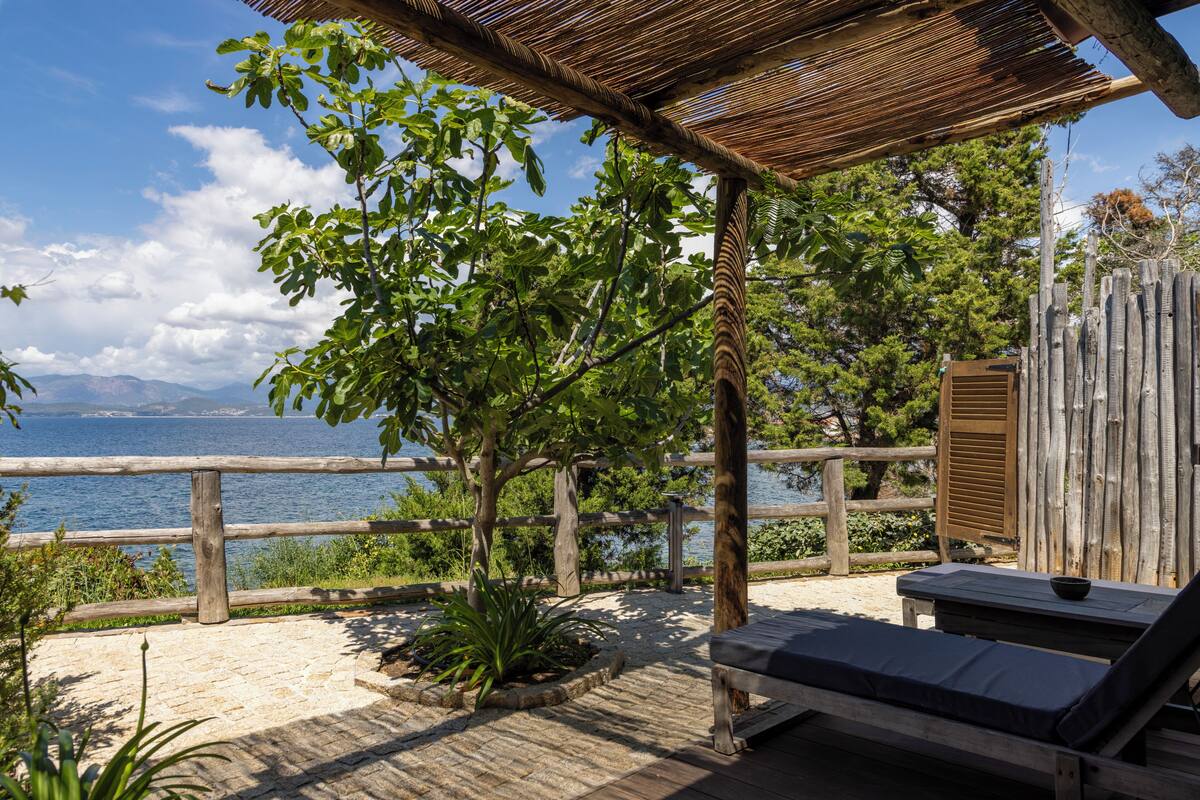 A wooden deck with a thatched roof, a wooden fence, and a lounge chair with a cushion.
