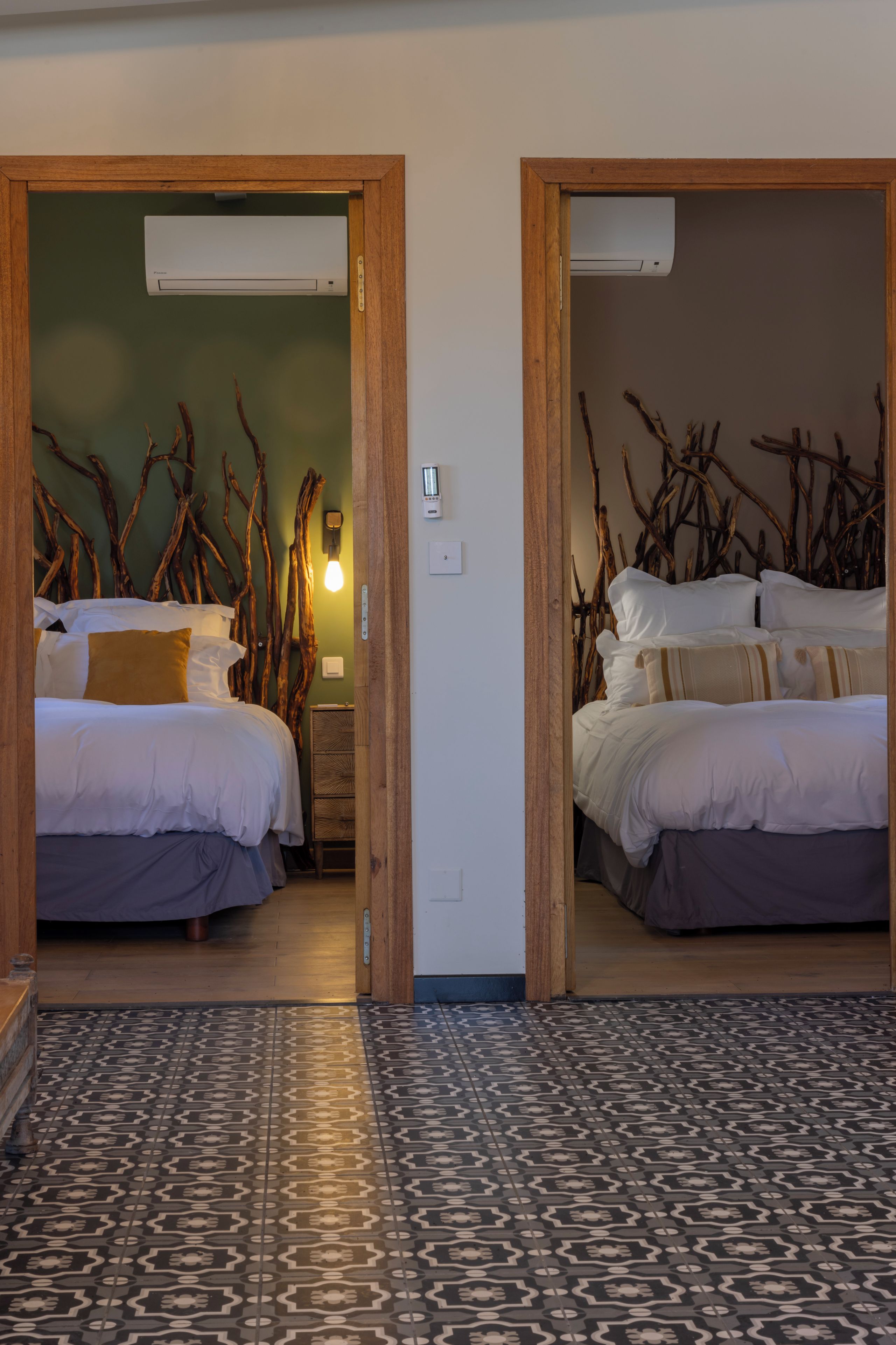 A hotel room with two beds, a patterned floor, and a wall decorated with branches.