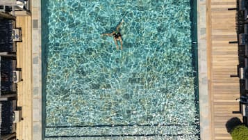 A square swimming pool with clear water, surrounded by wooden deck and lounge chairs.