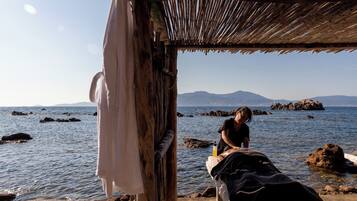 A beachside massage setup with a wooden structure, a towel, and a massage table by the water.
