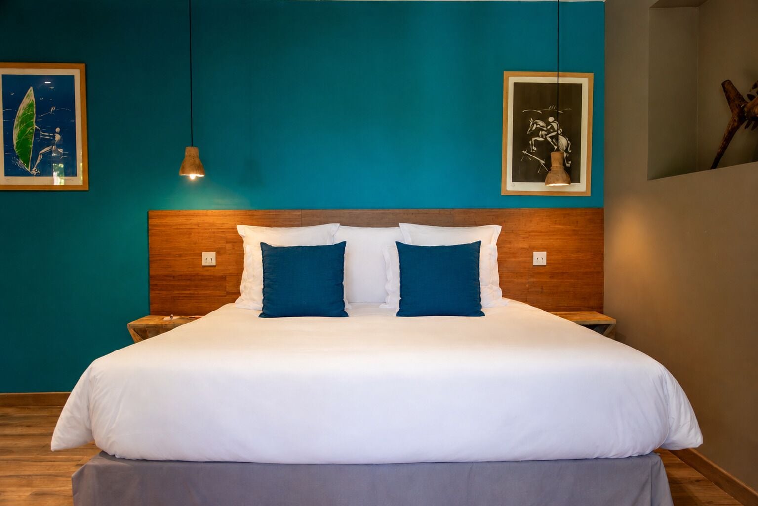 Una cama bien hecha con ropa de cama blanca y azul, un cabecero de madera y dos lámparas fijadas a la pared.