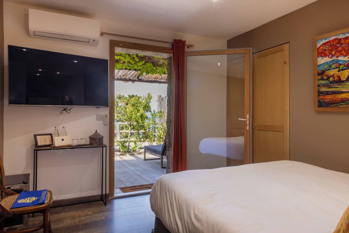 A bedroom with a bed, a TV, a desk with a laptop, and a door leading to an outdoor area.
