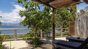 A wooden deck with a thatched roof, a wooden fence, and a lounge chair with a cushion.