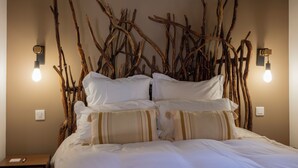 Una cama con ropa blanca, un aplique de pared y una rama de madera decorando la pared.