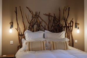 Una cama con ropa blanca, un aplique de pared y una rama de madera decorando la pared.