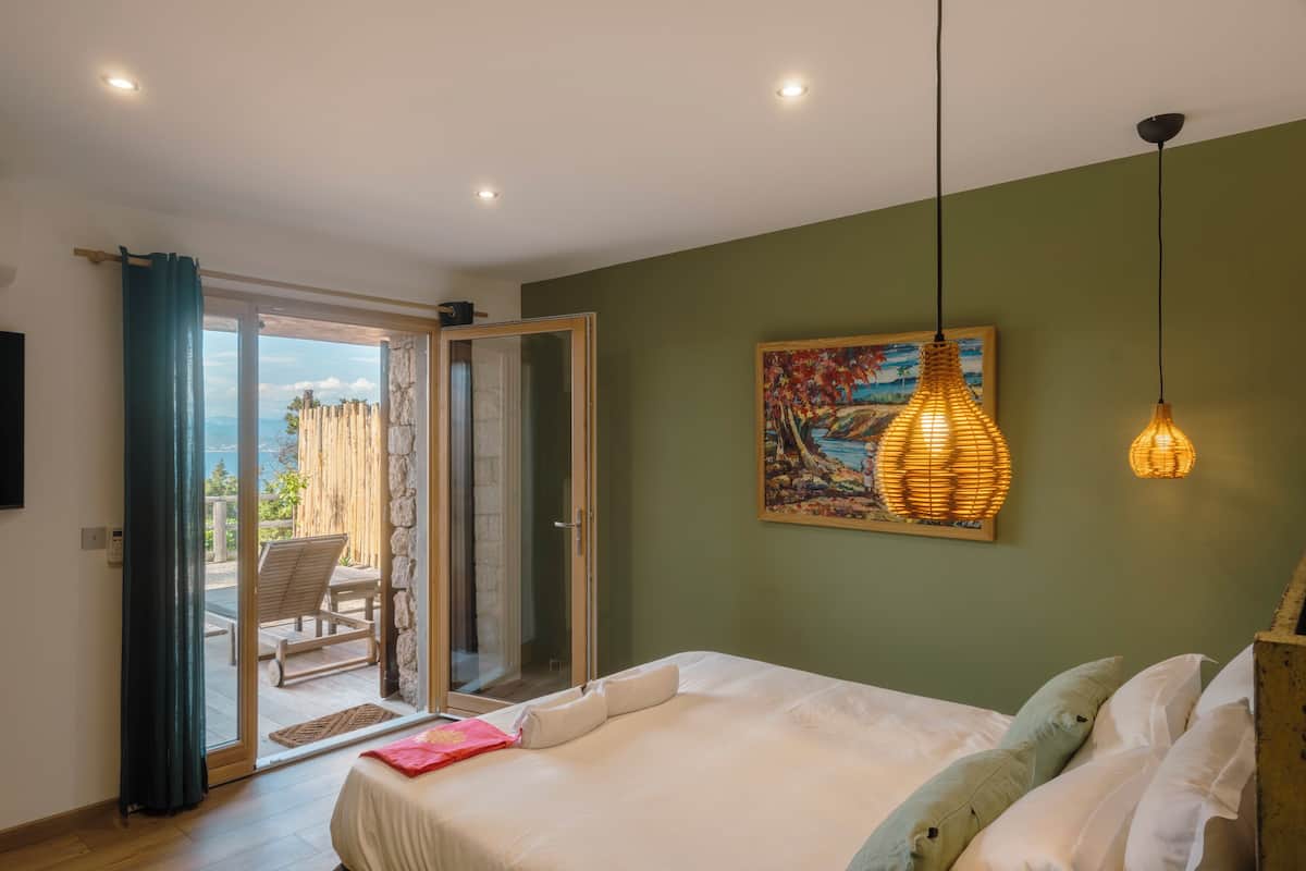 A bedroom with a bed, a painting, and a view through a glass door.