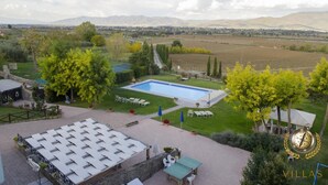 A pool area with lounge chairs and a table, surrounded by greenery and a view of distant mountains. - Villa Margherita (Cortona)