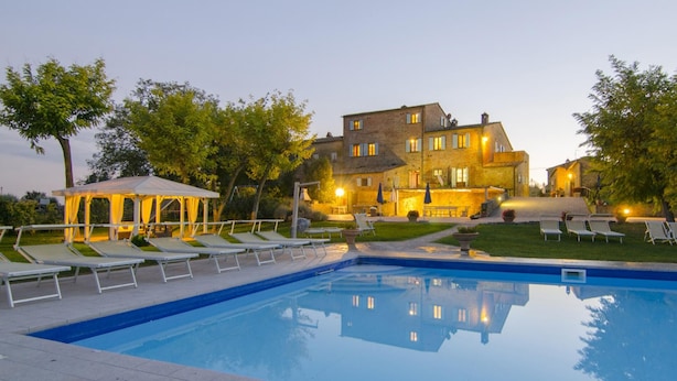 A pool area with lounge chairs, a gazebo, and a large building with multiple windows and lights. - Villa Margherita (Cortona)