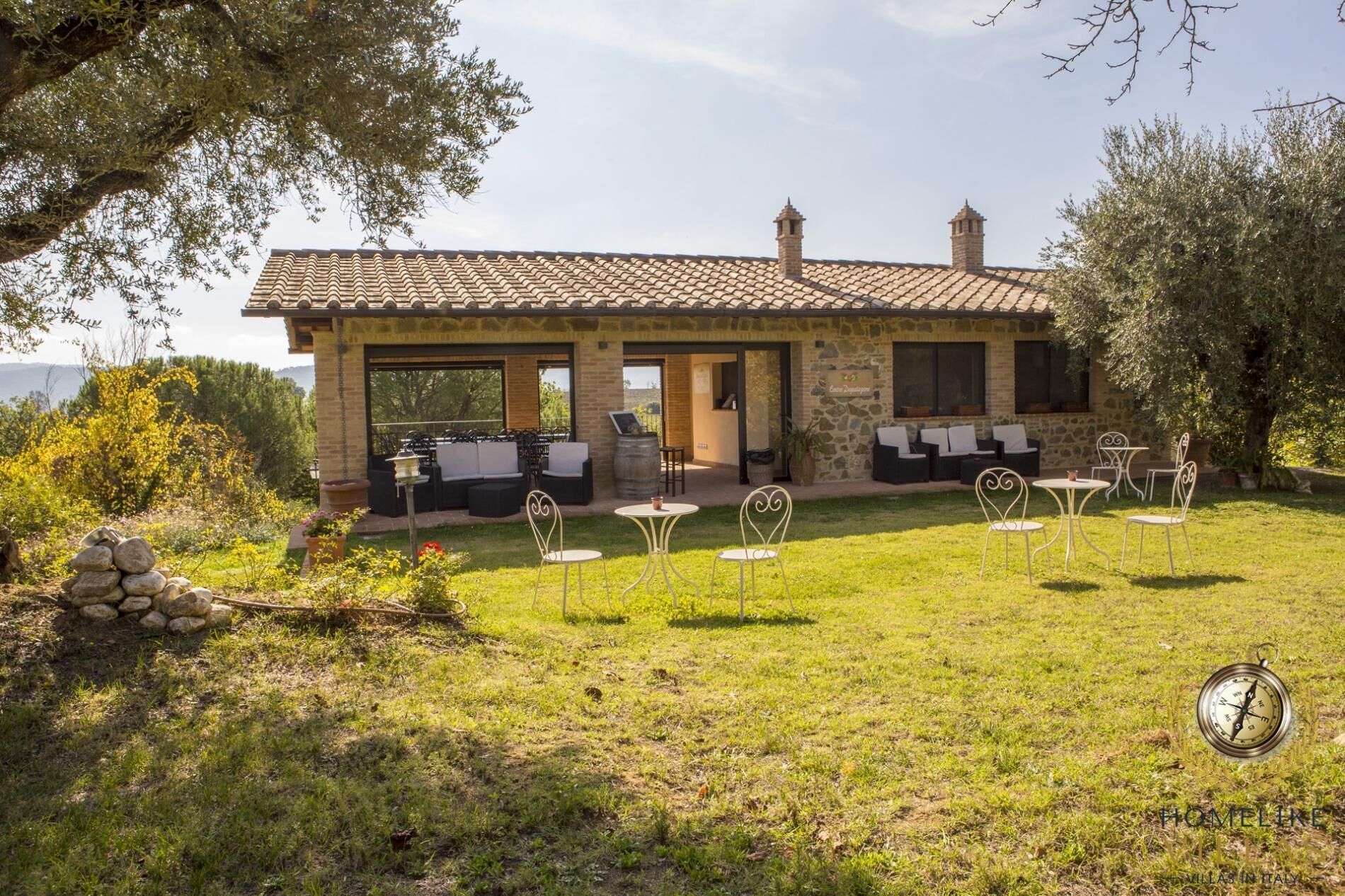 A stone building with a tiled roof, outdoor seating, and a grassy lawn.