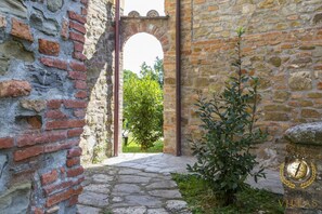 Walk through the historic entrance, flanked by ancient brick walls and a small shrub.