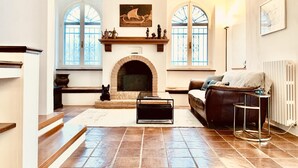A living room with a fireplace, a sofa, a coffee table, and two windows with decorative iron grills. - Villa Panperduto (Potenza Picena)